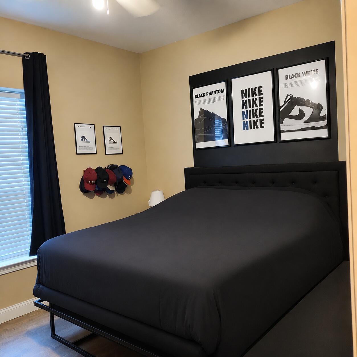 Bedroom with a large black bed, framed Nike sneaker posters, and baseball caps displayed on the wall.