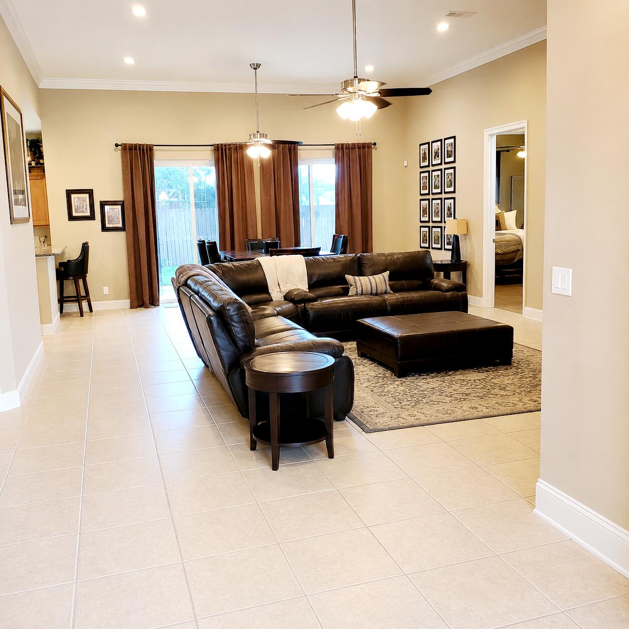 Furnished living room with a dark leather sectional, ottoman, and sliding glass doors.