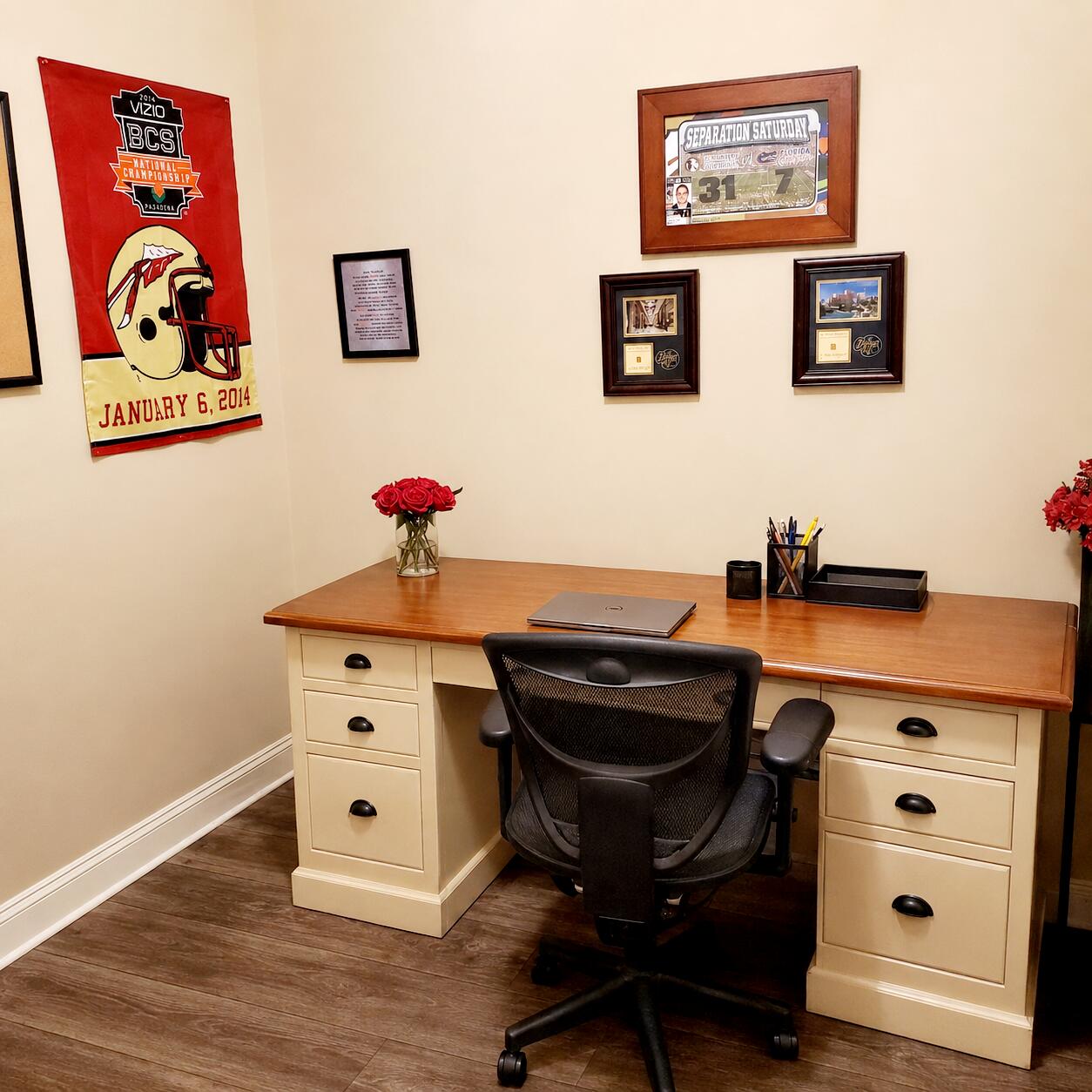 Home office with a wide desk, black swivel chair, and framed sports memorabilia.