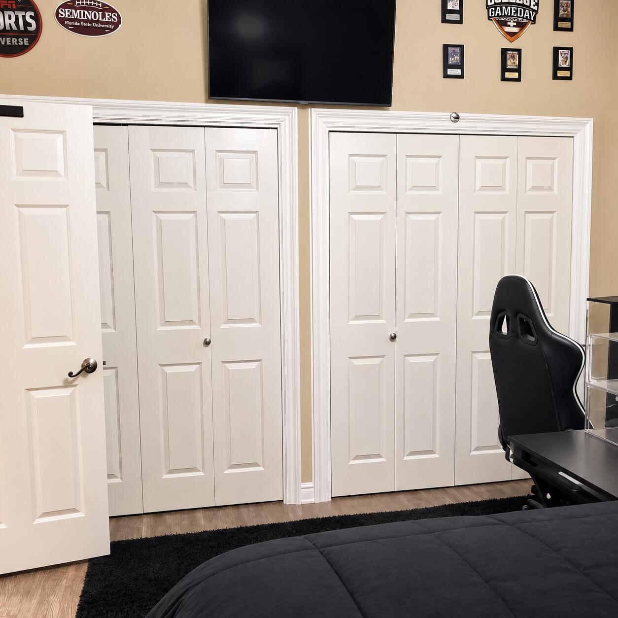 Bedroom with white paneled closets, a wall-mounted TV, and a black gaming chair beside the bed.