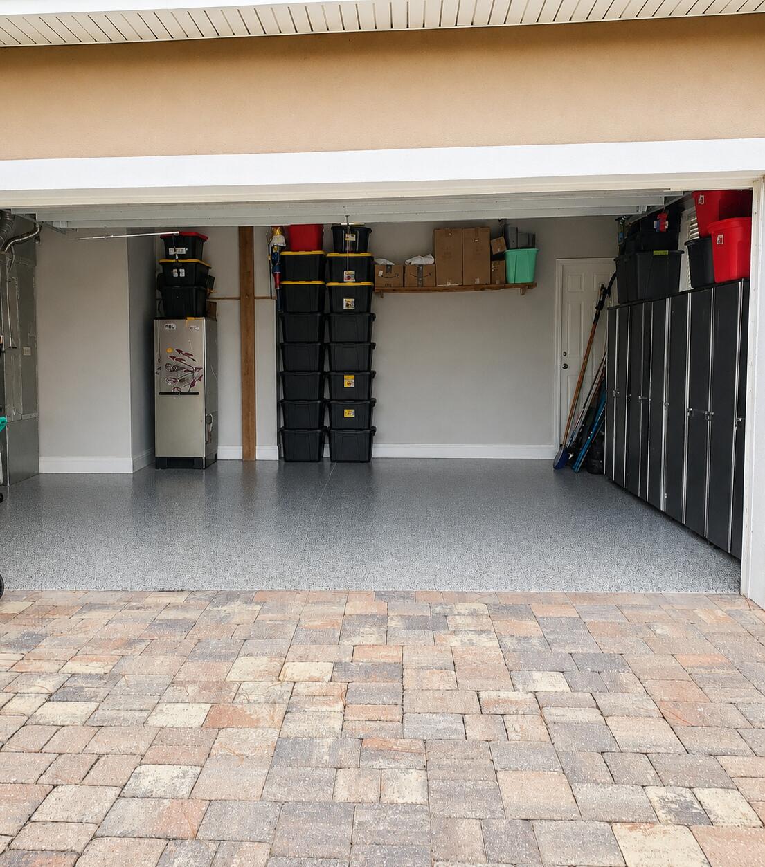 Garage with a speckled gray floor, stacked storage bins, and wall cabinets.