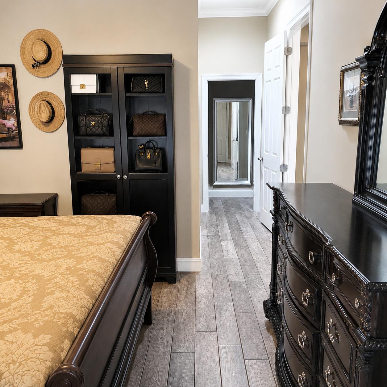 Bedroom with an ornate dark wood bed, gold floral bedspread, and cabinet displaying handbags.