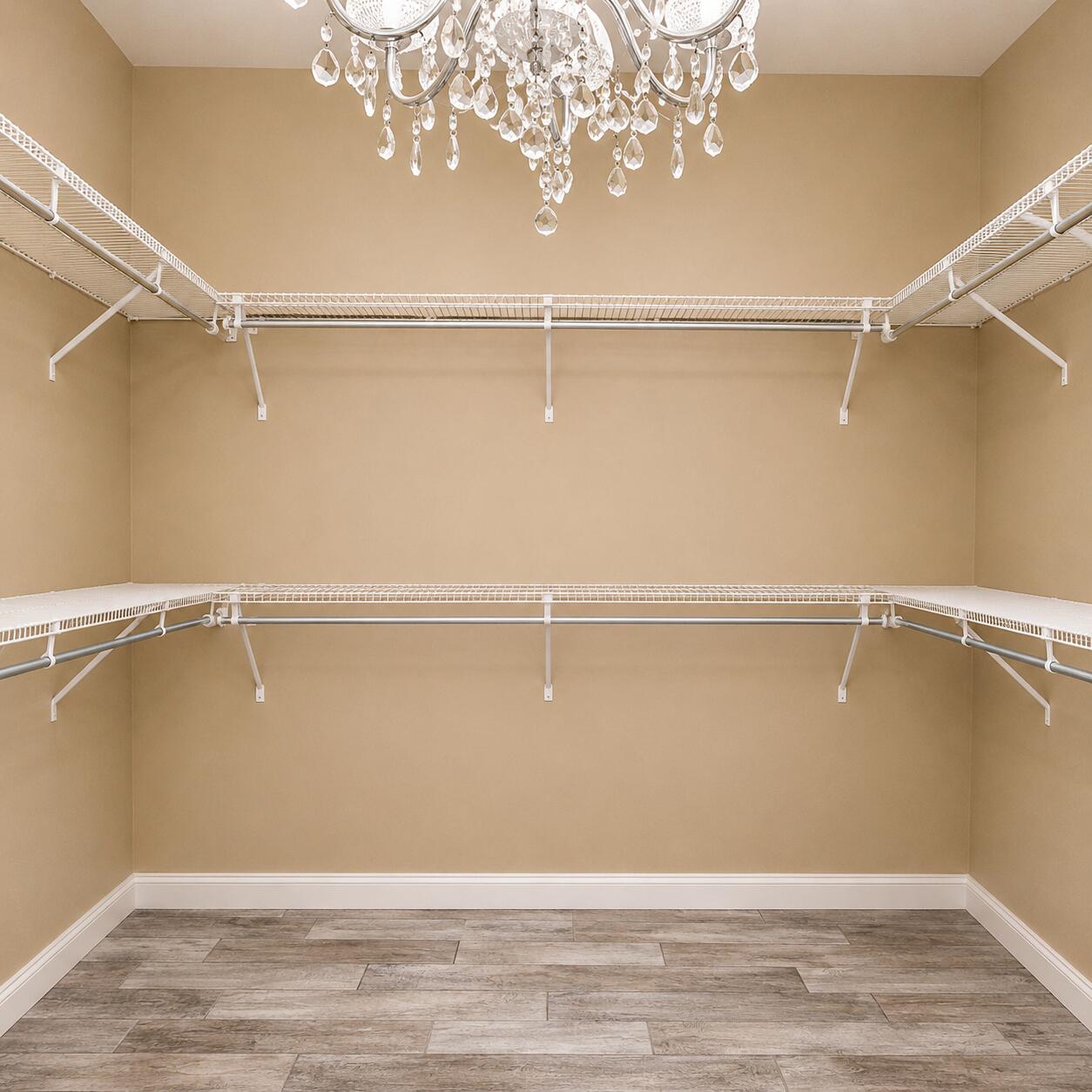 Empty walk-in closet with wraparound white shelving, a crystal chandelier, and wood-look tile flooring.