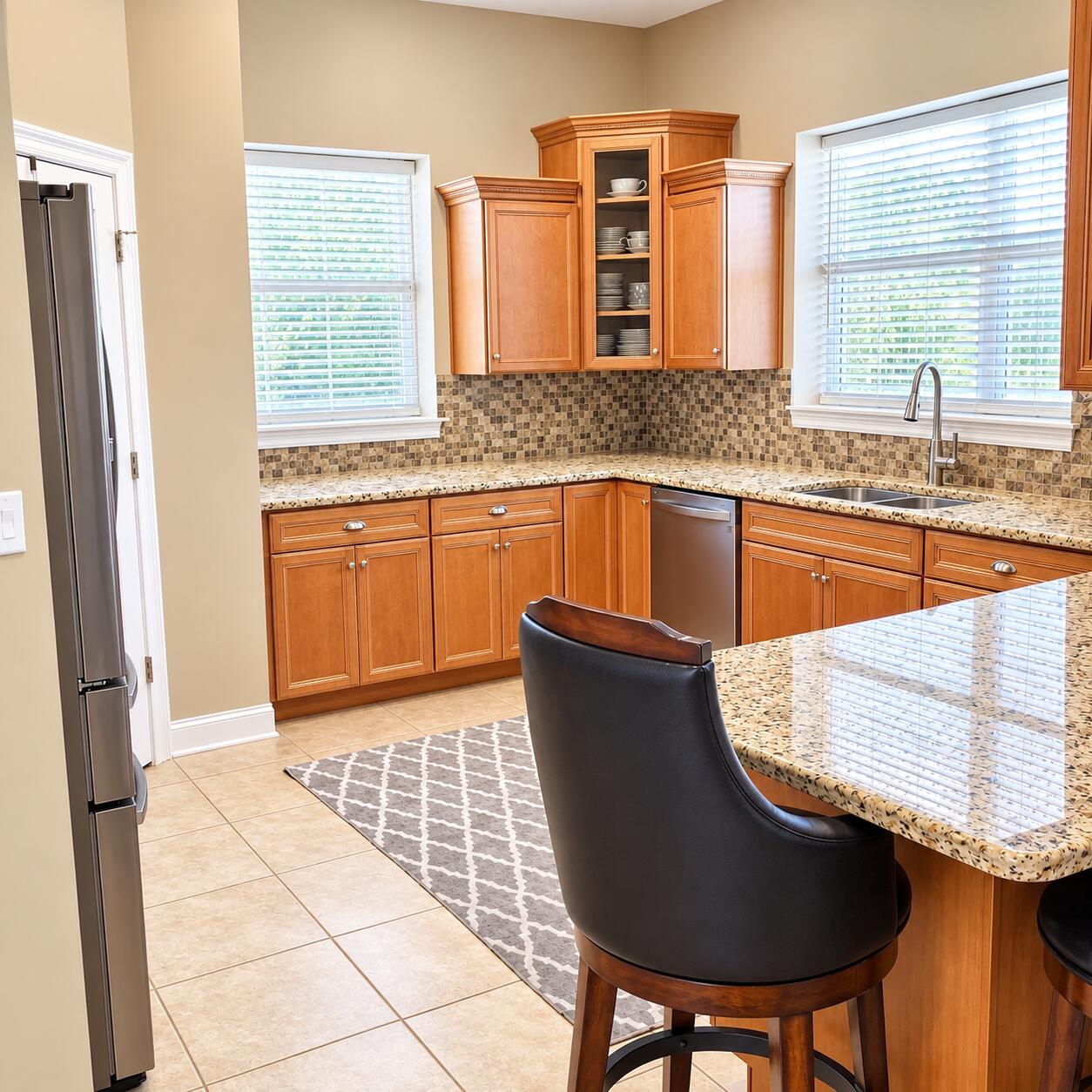 Kitchen with warm wood cabinets, mosaic backsplash, granite counters, and a breakfast bar with dark stools.