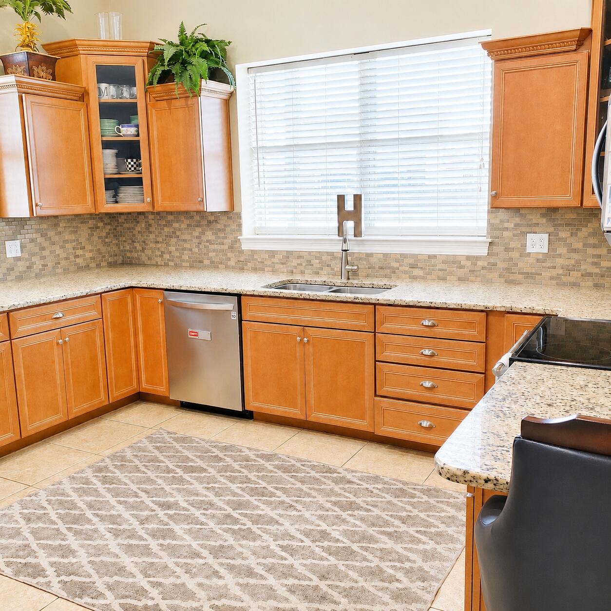 Kitchen with honey-colored cabinets, mosaic backsplash, double sink, and patterned rug.