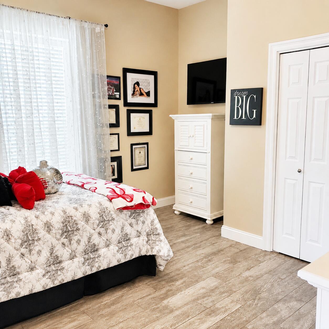 Bedroom with floral bedding, red accents, a white dresser, and a wall-mounted television.