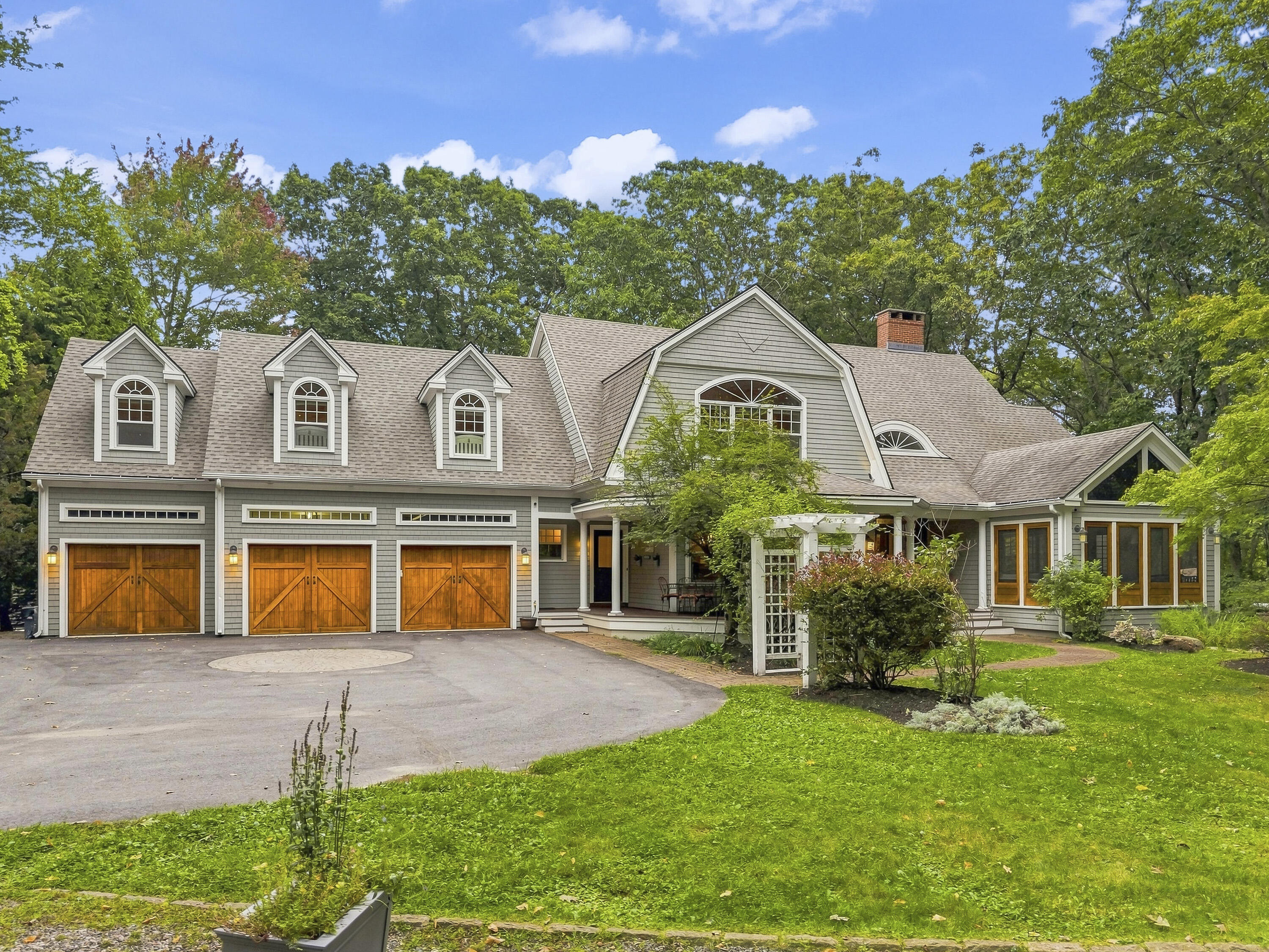 Gray shingle-sided home with three wooden garage doors, dormers, and a landscaped front lawn.