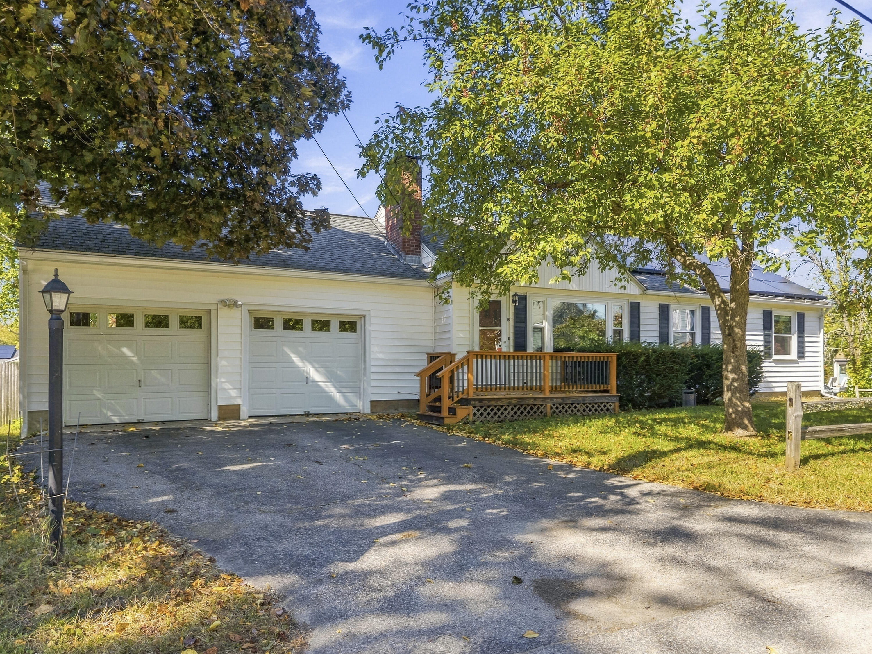 White single-story home with a two-car garage and wooden front deck beneath mature autumn trees.