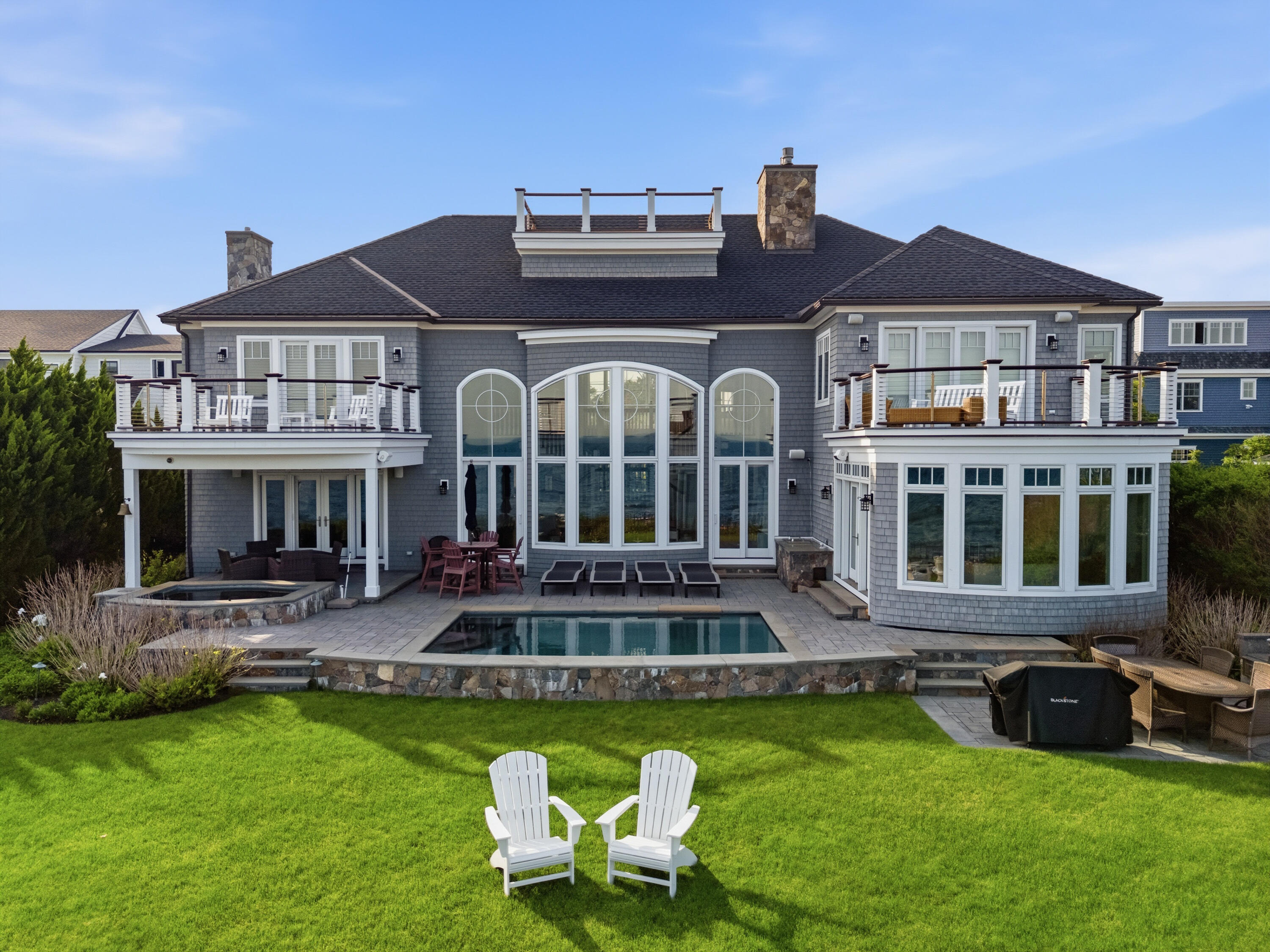 Gray-shingled house with two decks, a swimming pool, and Adirondack chairs on the lawn.