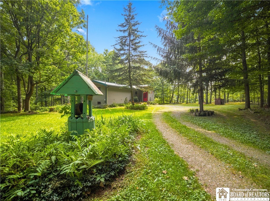 Small house with a red door on a wooded lot, with a gravel drive and green-roofed well structure.