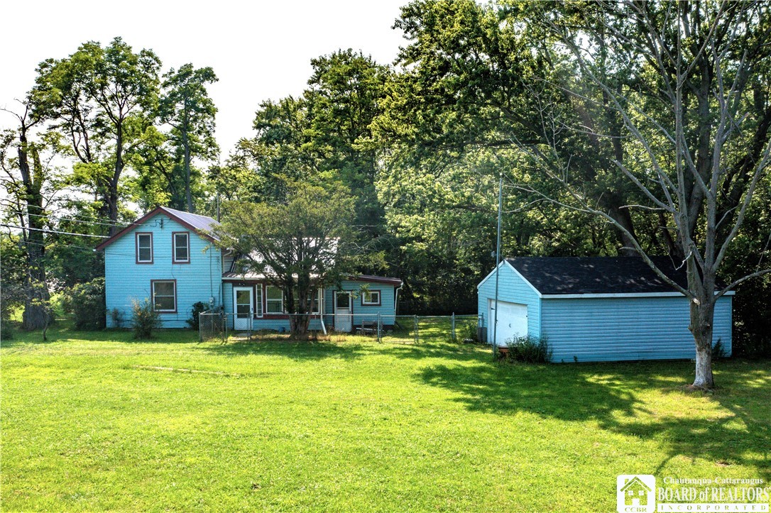 Blue two-story house and detached garage surrounded by a broad lawn and mature trees.