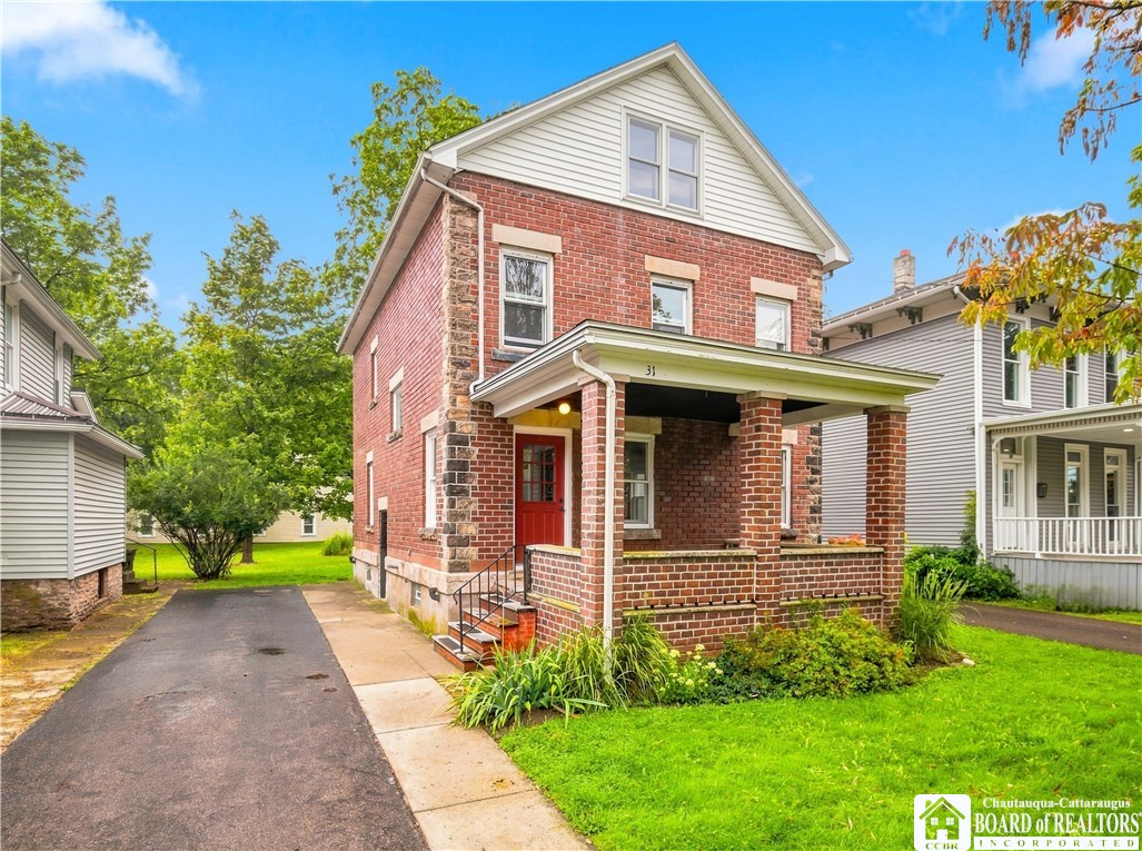 Two-story red brick house with a covered porch, red front door, and side driveway.