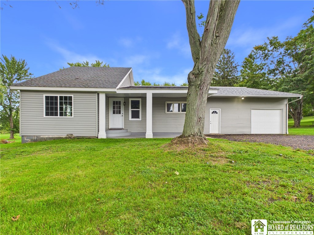 Gray single-story house with an attached garage, covered entry, and large tree in the front lawn.