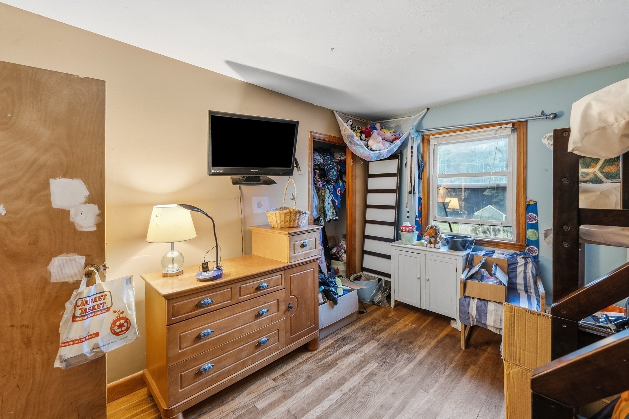 Cluttered bedroom with a wooden dresser, clothes-filled closet, window, and bunk bed.