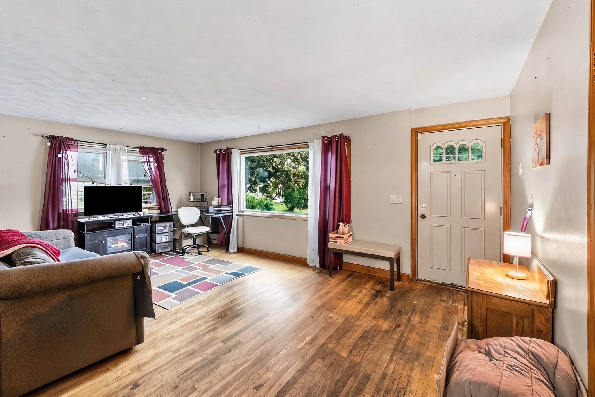 Living room with hardwood floors, purple curtains, and a front door with a three-pane window.