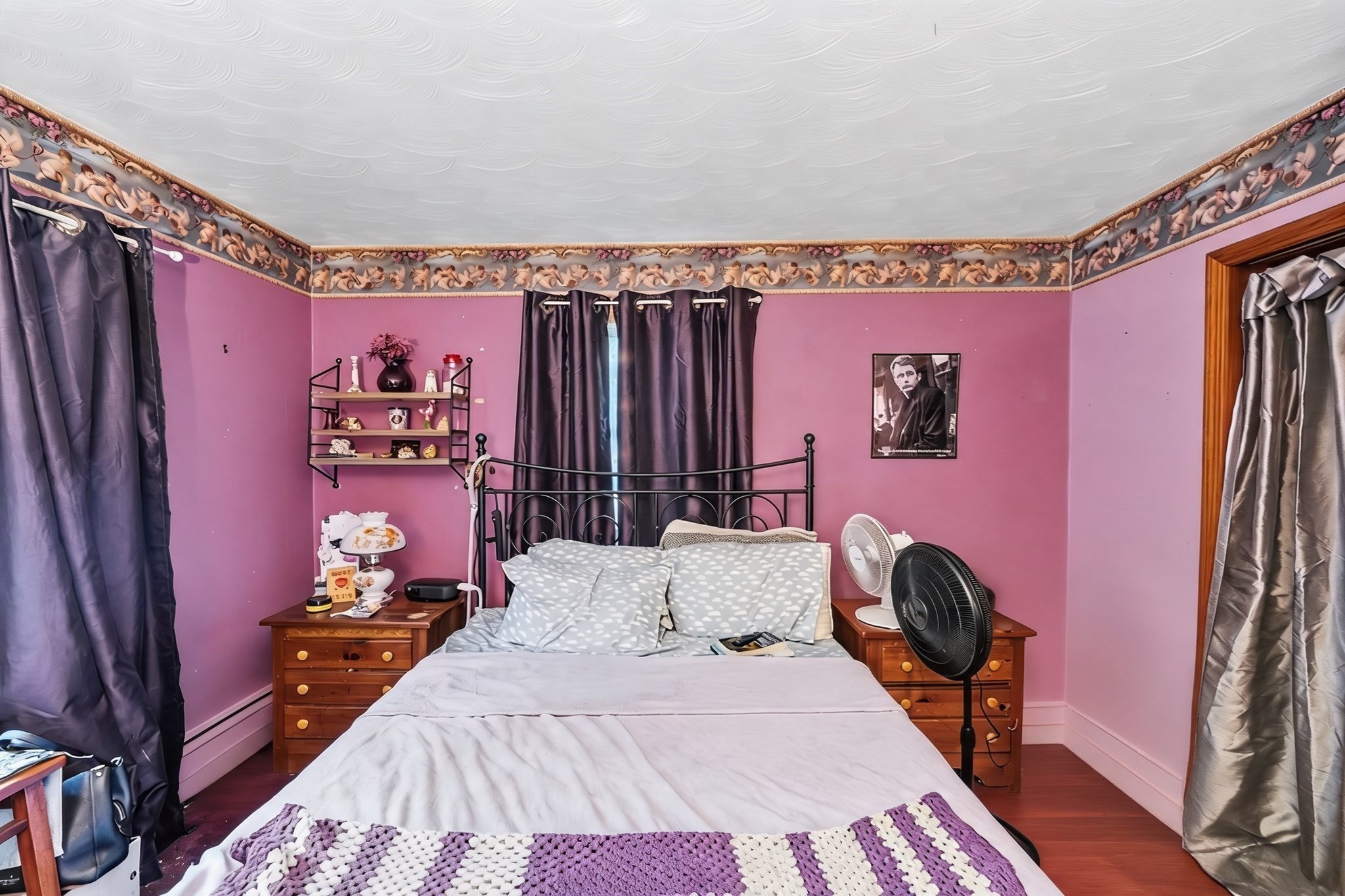 Bedroom with pink walls, a black metal bed, dark curtains, and a purple-and-white crocheted blanket.