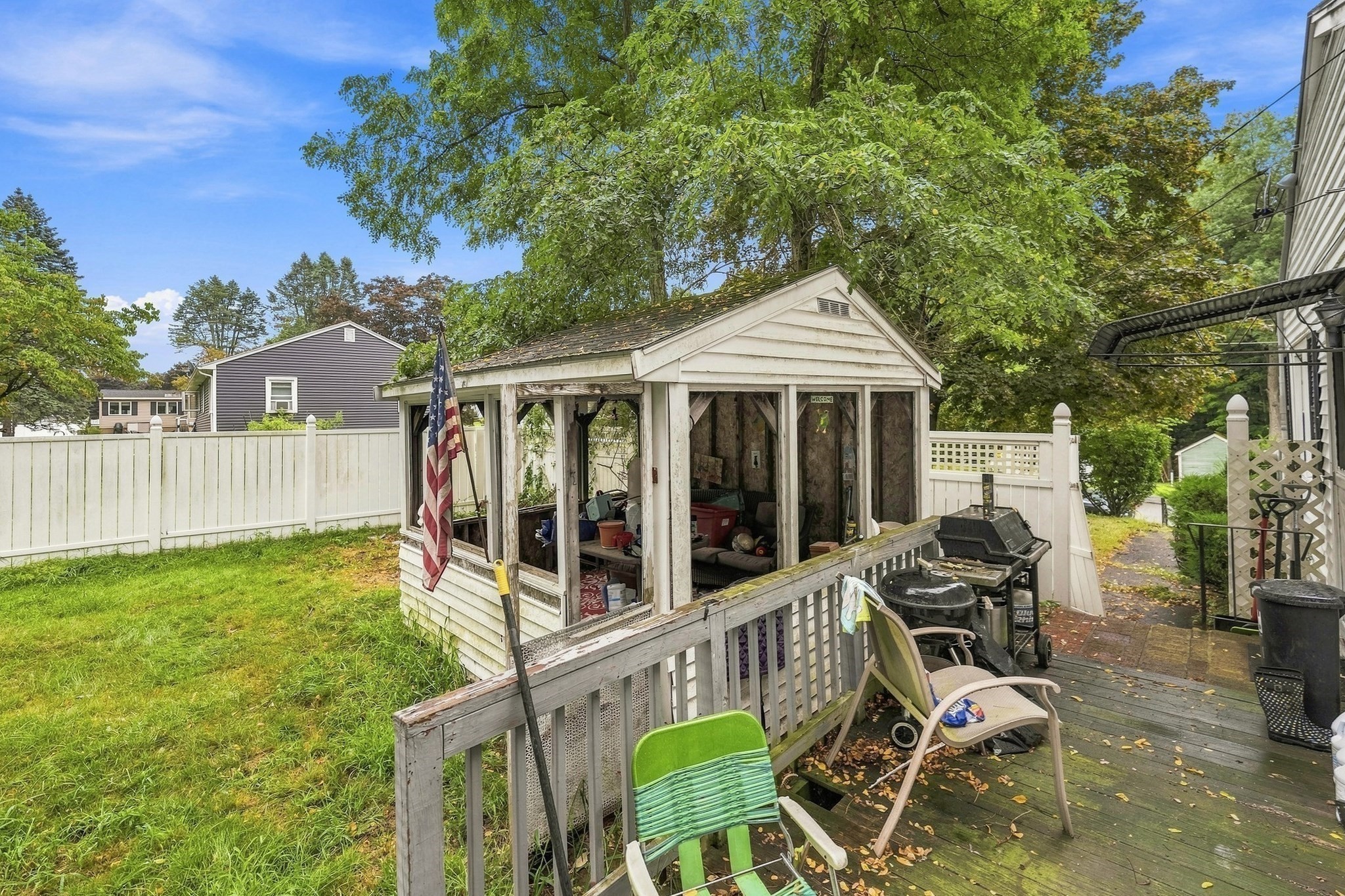 Backyard deck with a screened gazebo, outdoor chairs, grills, and a fenced lawn.