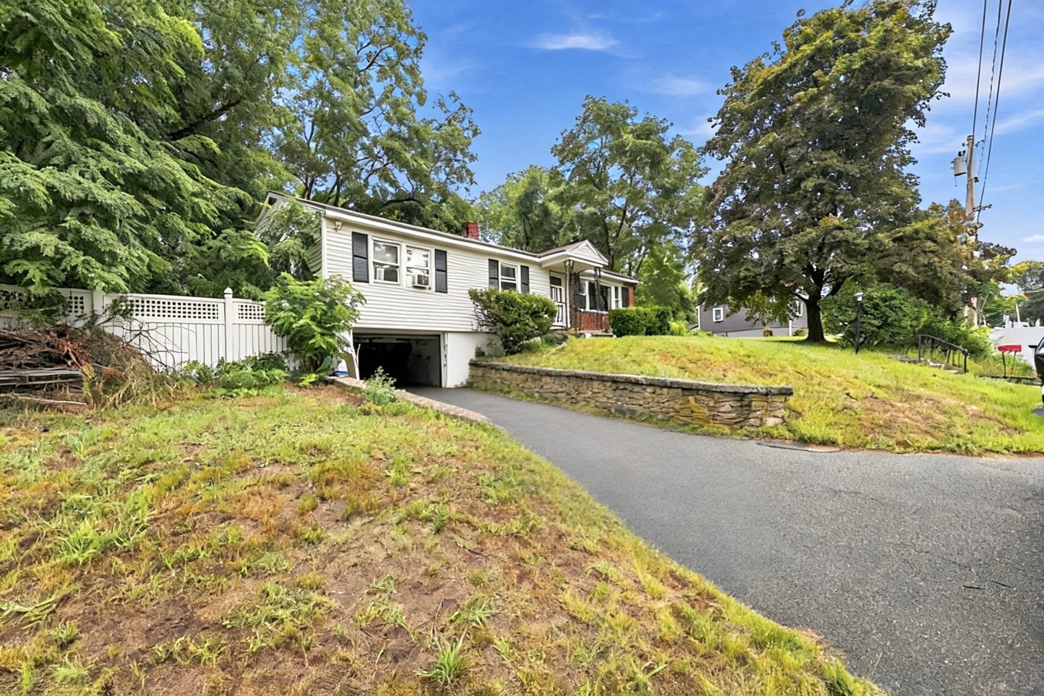 White raised ranch with an attached garage, driveway, lattice fence, and stone retaining wall.