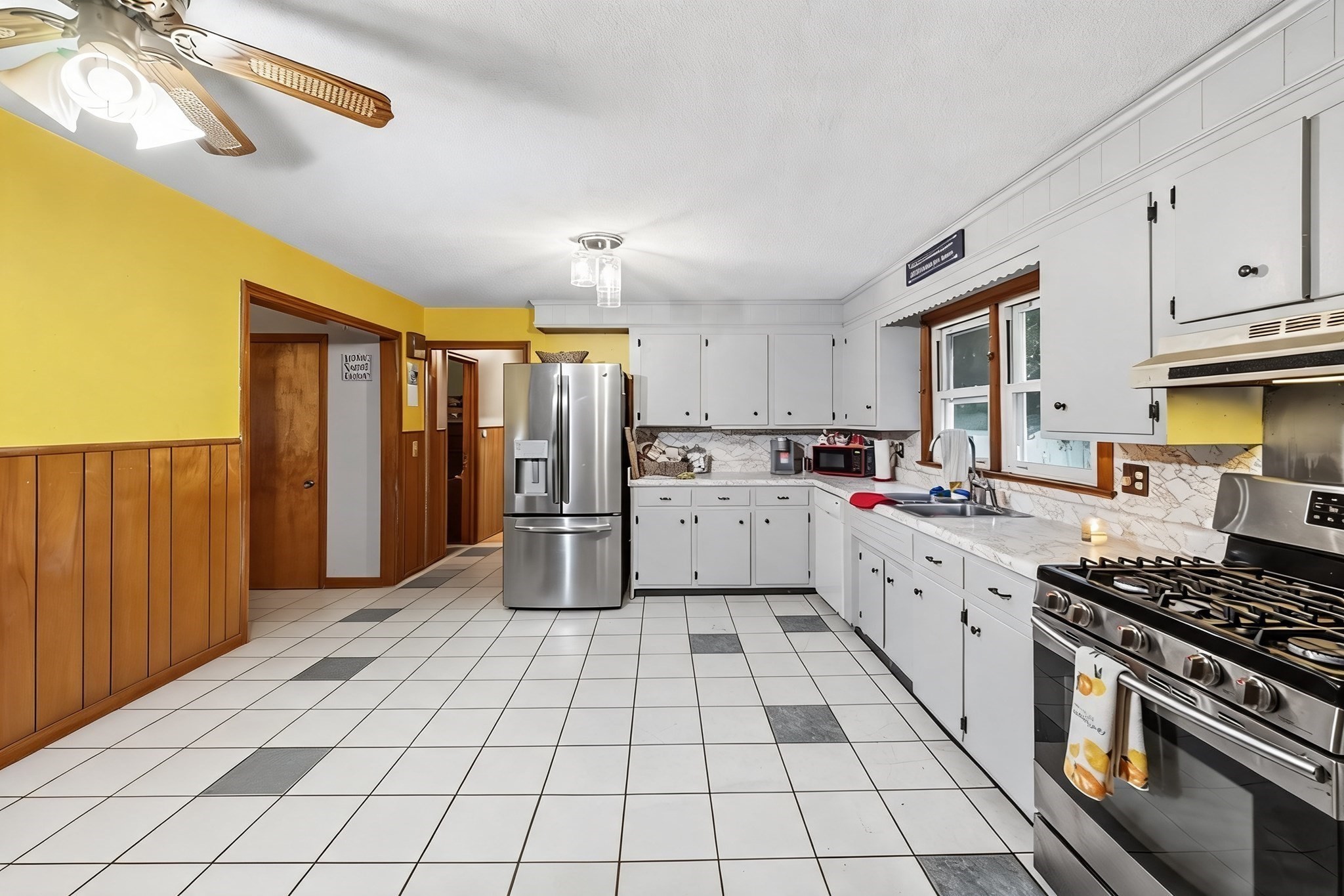 Kitchen with white cabinets, stainless-steel appliances, yellow walls, and a tiled floor.