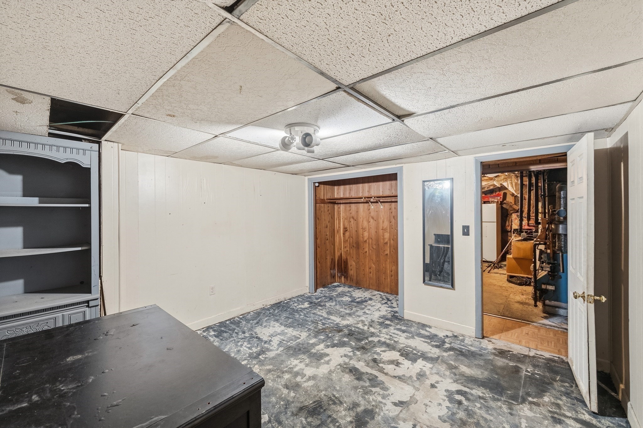 Basement room with built-in shelving, a wood-paneled closet, and an open doorway to the utility area.