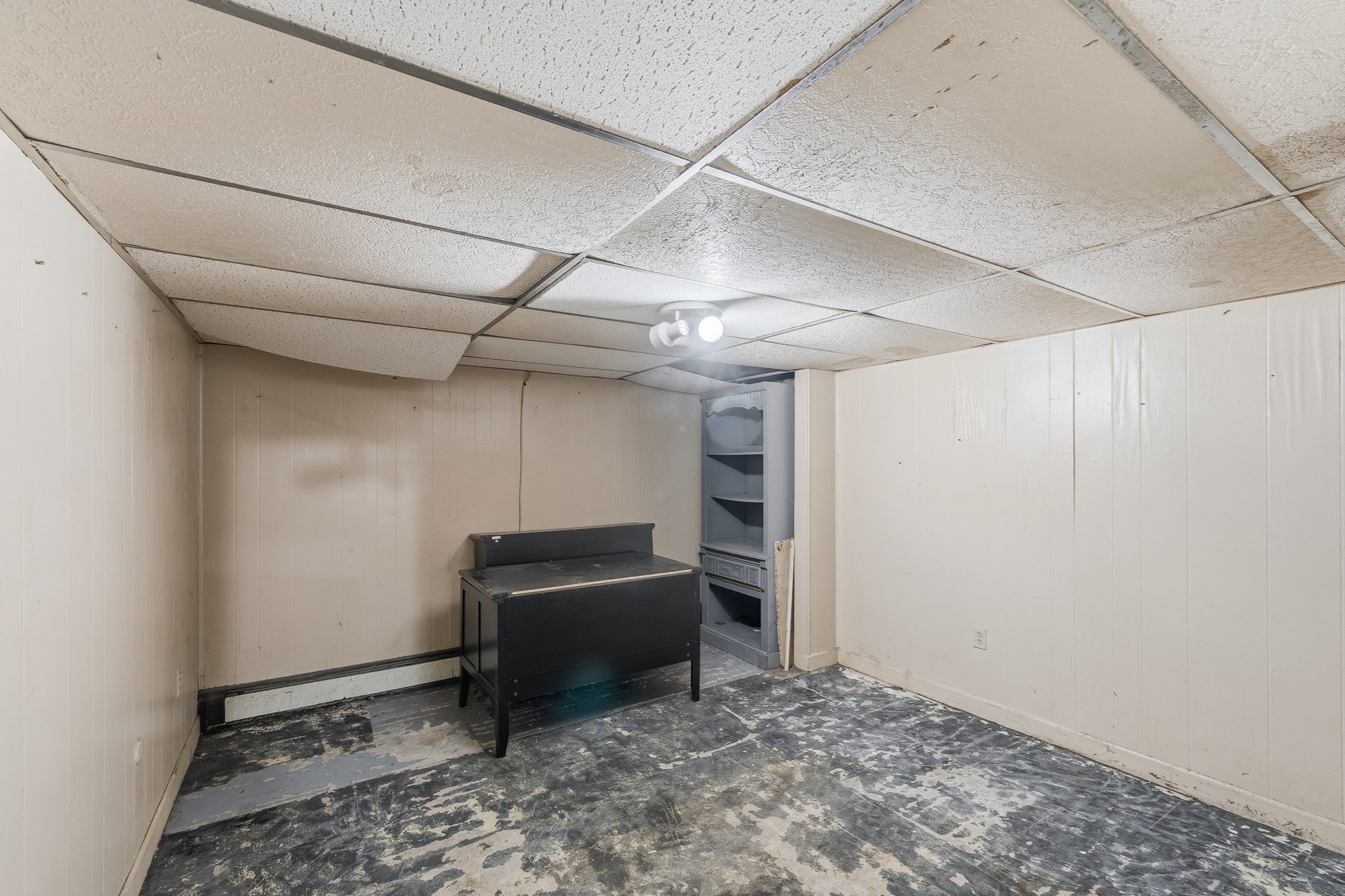 Unfinished basement with a black workbench, built-in shelving, and worn concrete floor.