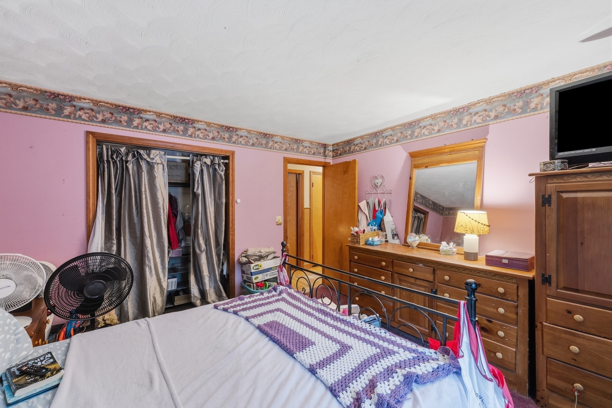 Bedroom with pink walls, a metal bed, and a long wooden dresser beneath a mirror.