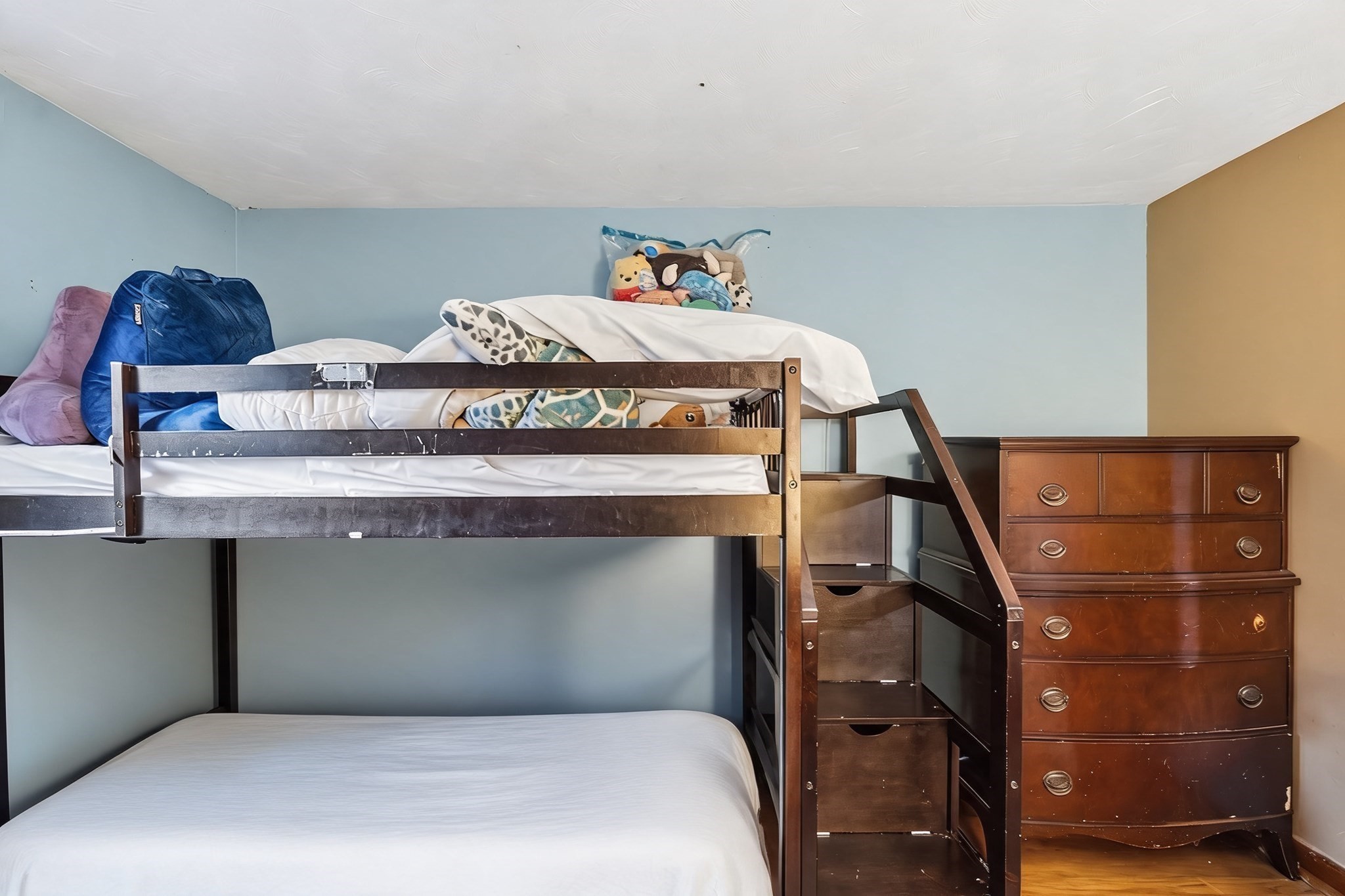 Bedroom with a wooden bunk bed, built-in stairs and drawers, and a matching dresser.