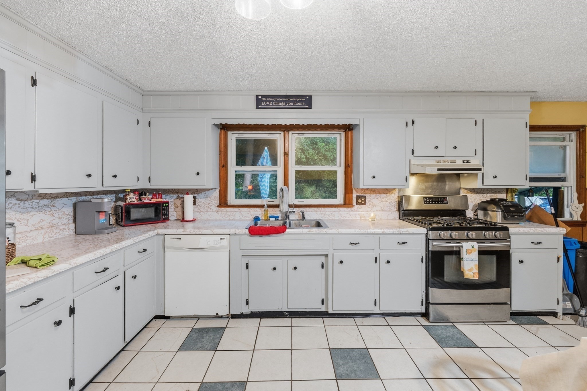 Kitchen with white cabinets, a stainless-steel gas range, and a sink beneath a wood-trimmed window.