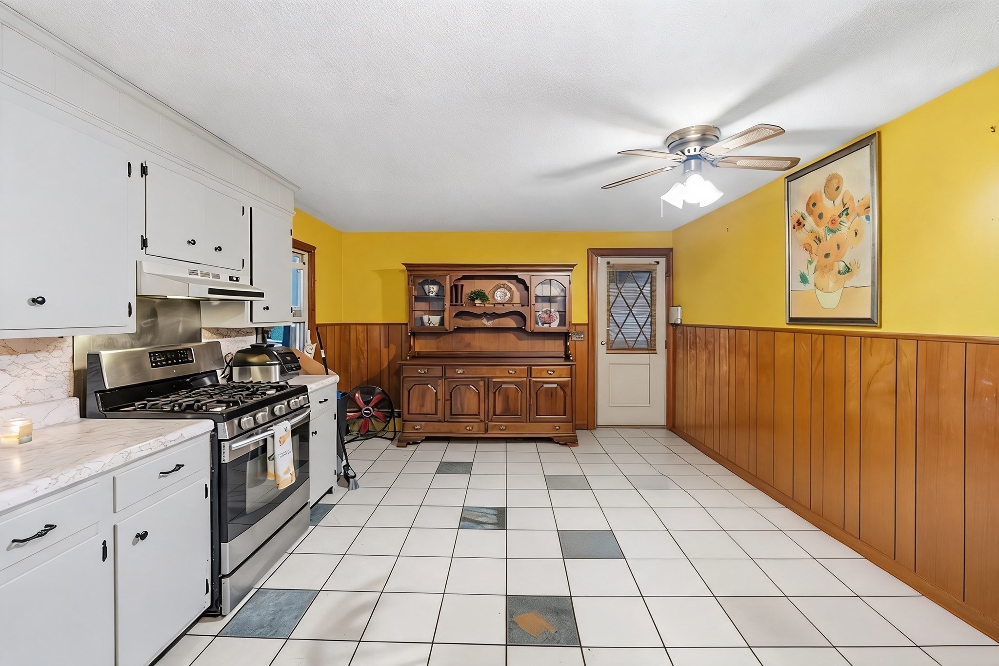 Kitchen with a stainless steel gas range, yellow walls, wood paneling, and a large wooden hutch.