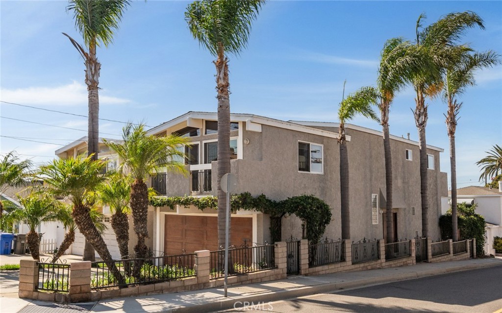 Two-story stucco home with a wood garage door, iron fencing, and palm trees.