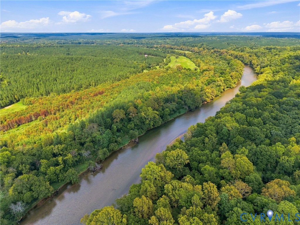 Aerial view of a winding river through dense woodland, with a small clearing in the distance.