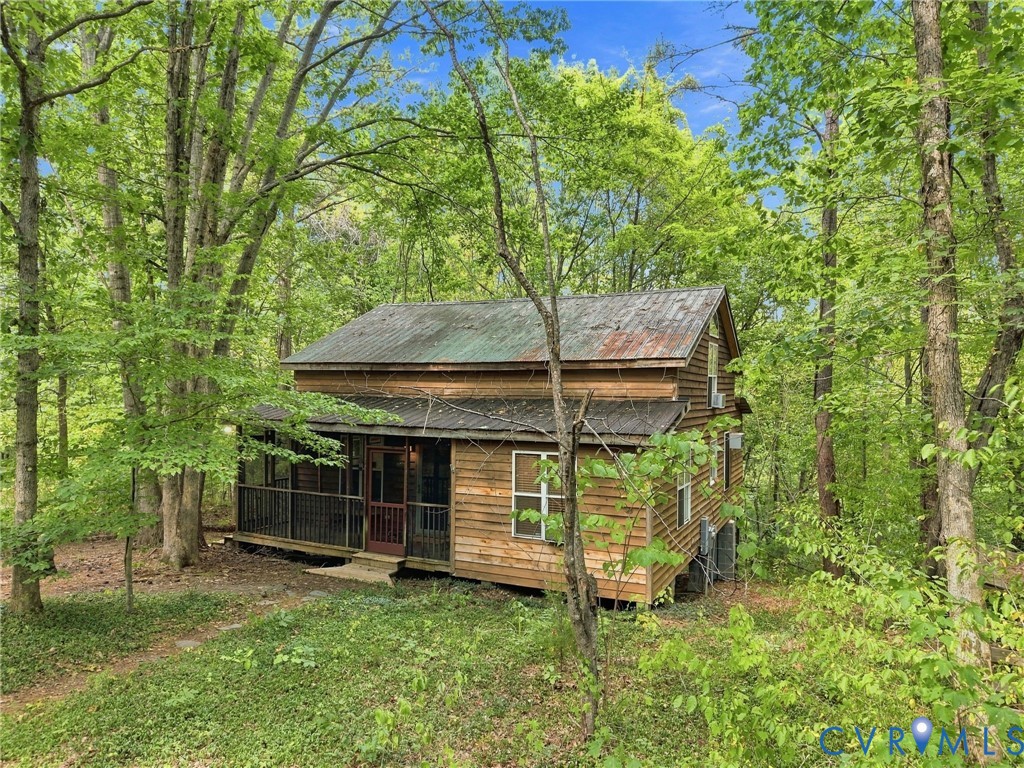 Wood-sided cabin with a metal roof and covered porch nestled among trees.