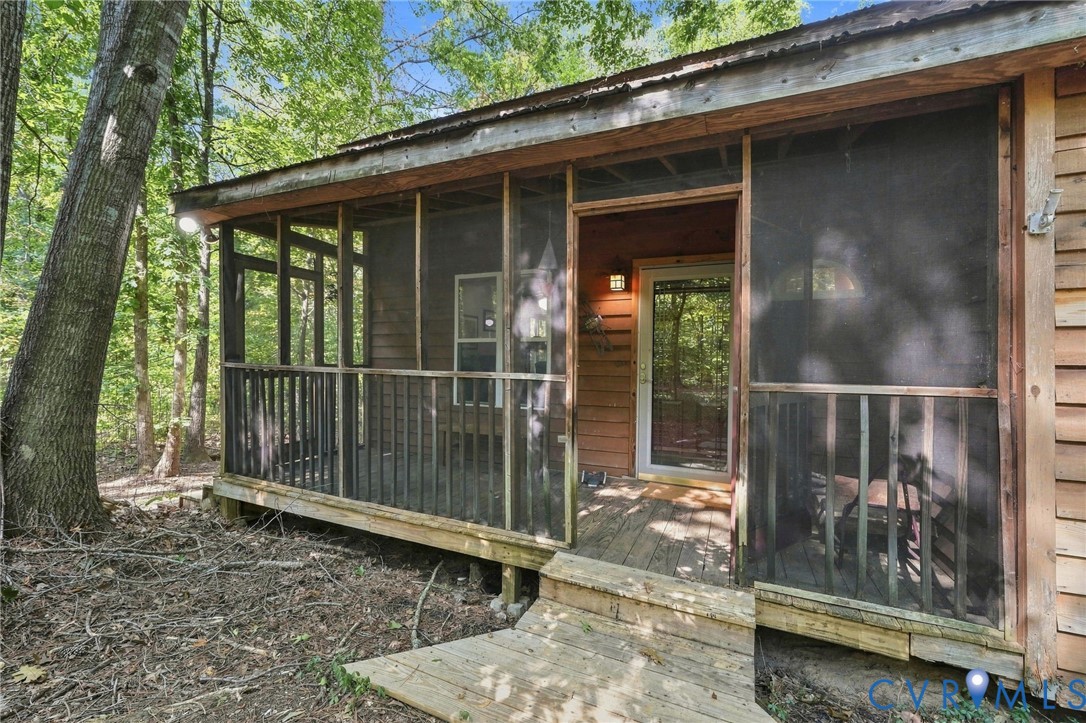 Wood-sided home with a screened porch and deck steps nestled among mature trees.