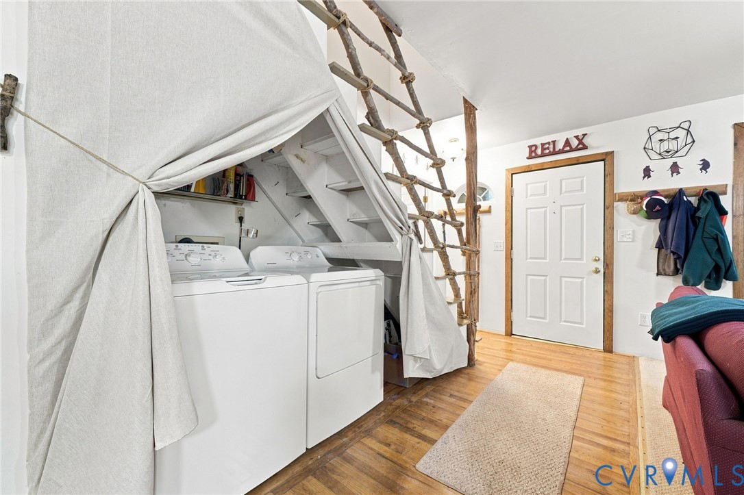 Laundry area with washer and dryer beneath a staircase, beside an entry door and seating.