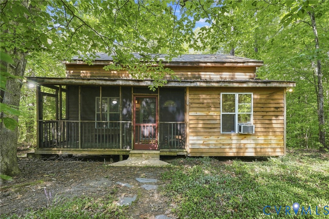Wood-sided cabin among trees with a covered screened porch and gravel approach.