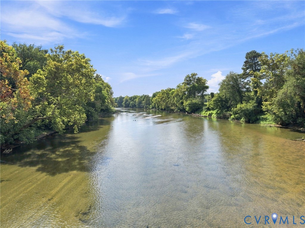 Broad river bordered by dense green trees under a bright blue sky.