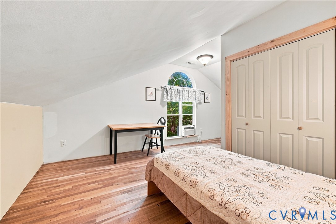Bedroom with sloped ceiling, hardwood floors, arched window, desk, and large closet.