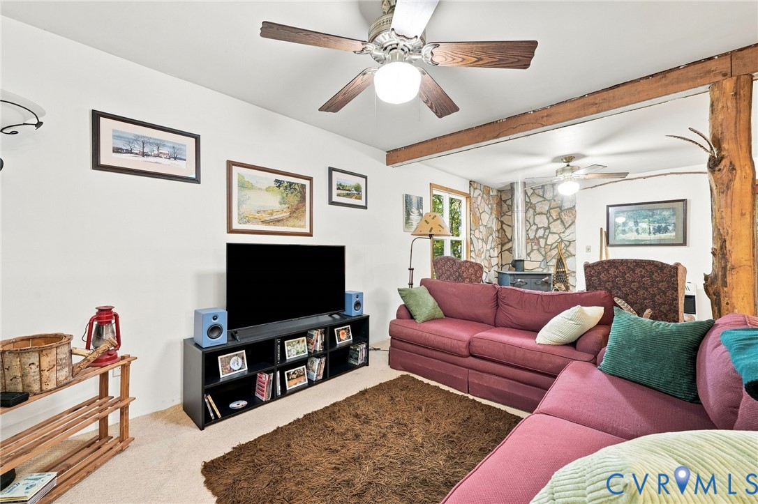 Furnished living room with pink sectional sofas, exposed beams, and a stone wall with a wood-burning stove.