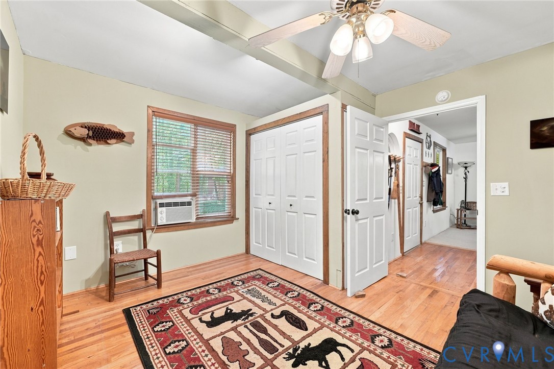 Furnished room with wood floors, white closet doors, a window air conditioner, and a patterned rug.