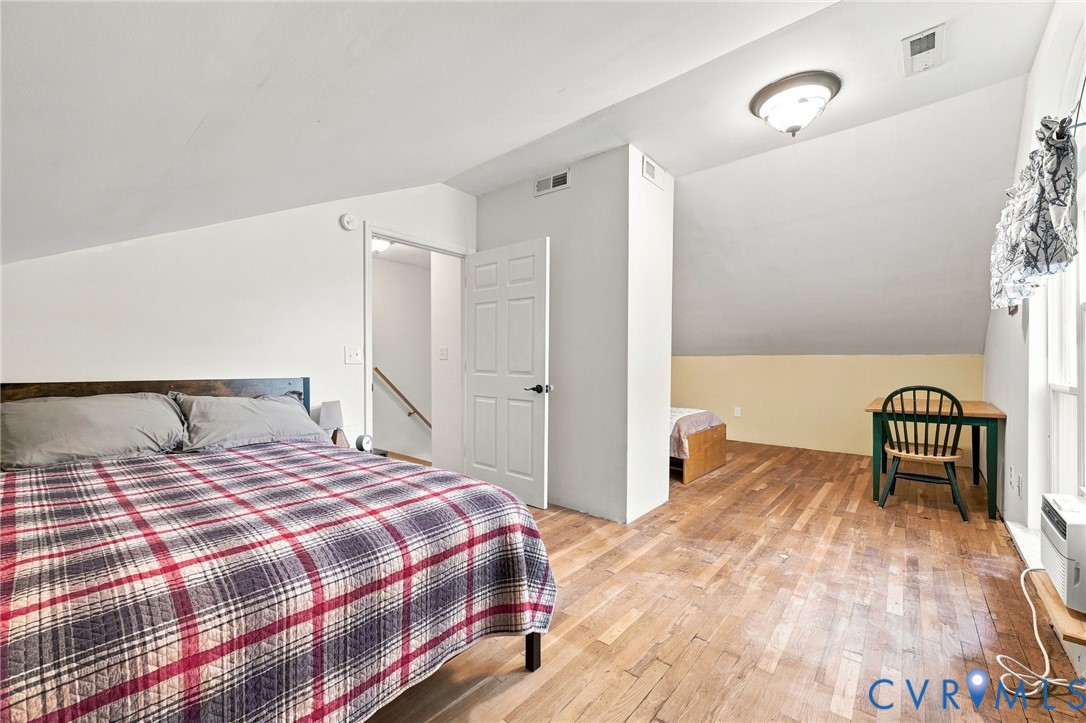 Bedroom with hardwood floors, sloped ceiling, two beds, and a desk by the window.