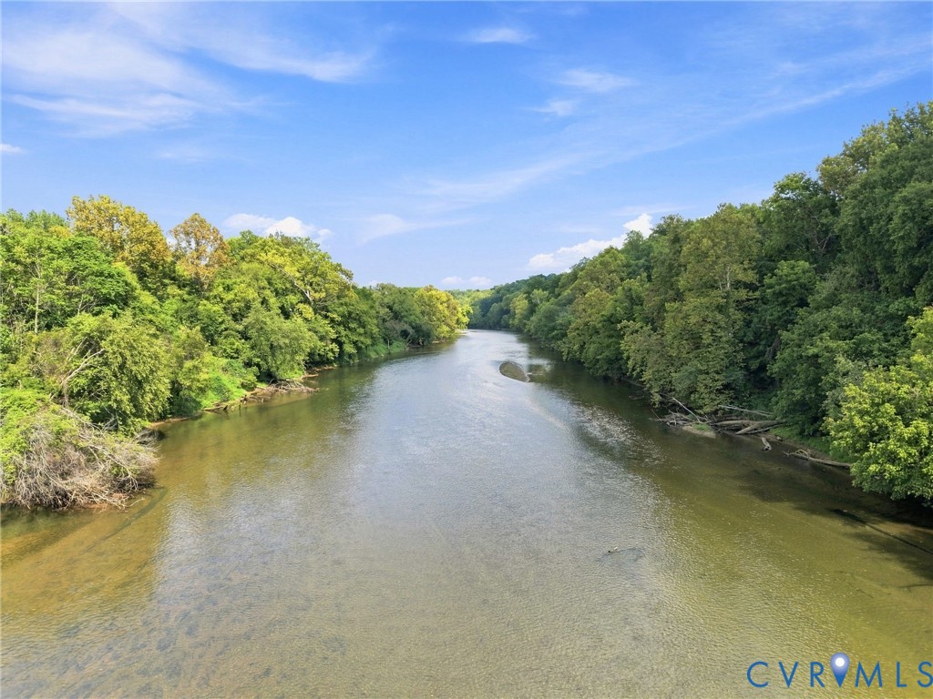 River bordered by wooded banks beneath a bright blue sky.