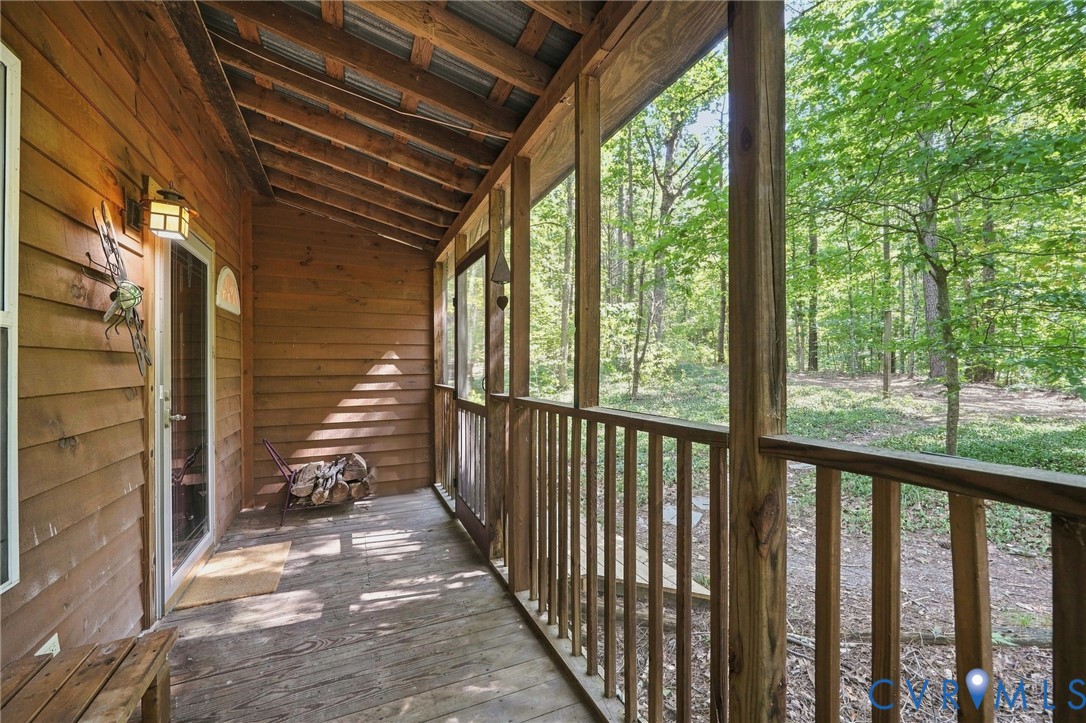 Covered wooden porch with a glass-paneled door and wooded views through the railing.