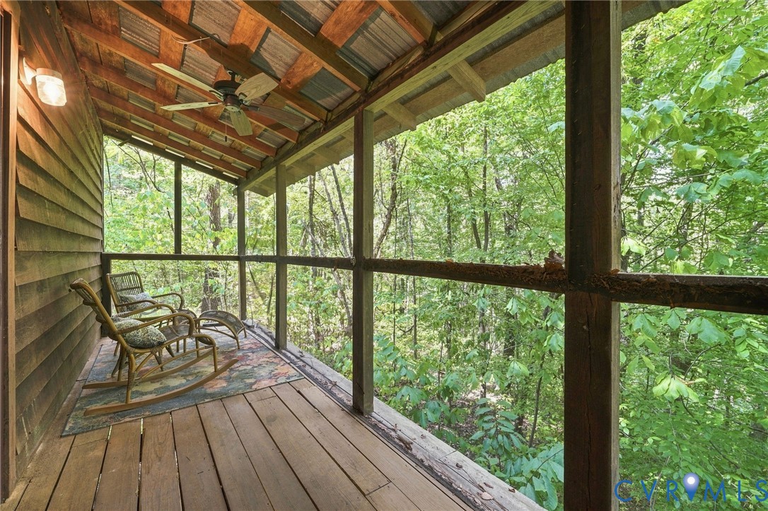 Covered wooden porch with rocking chairs and a ceiling fan overlooking dense woodland.