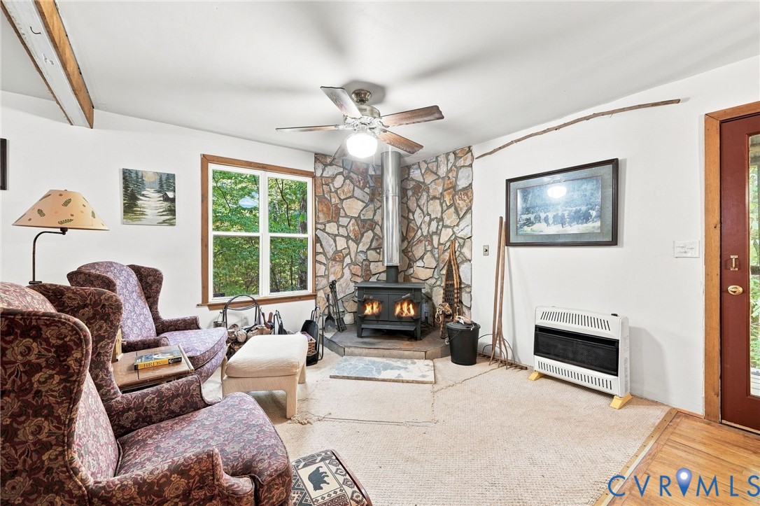 Living room with a stone fireplace, wood-burning stove, patterned armchairs, and a large window.