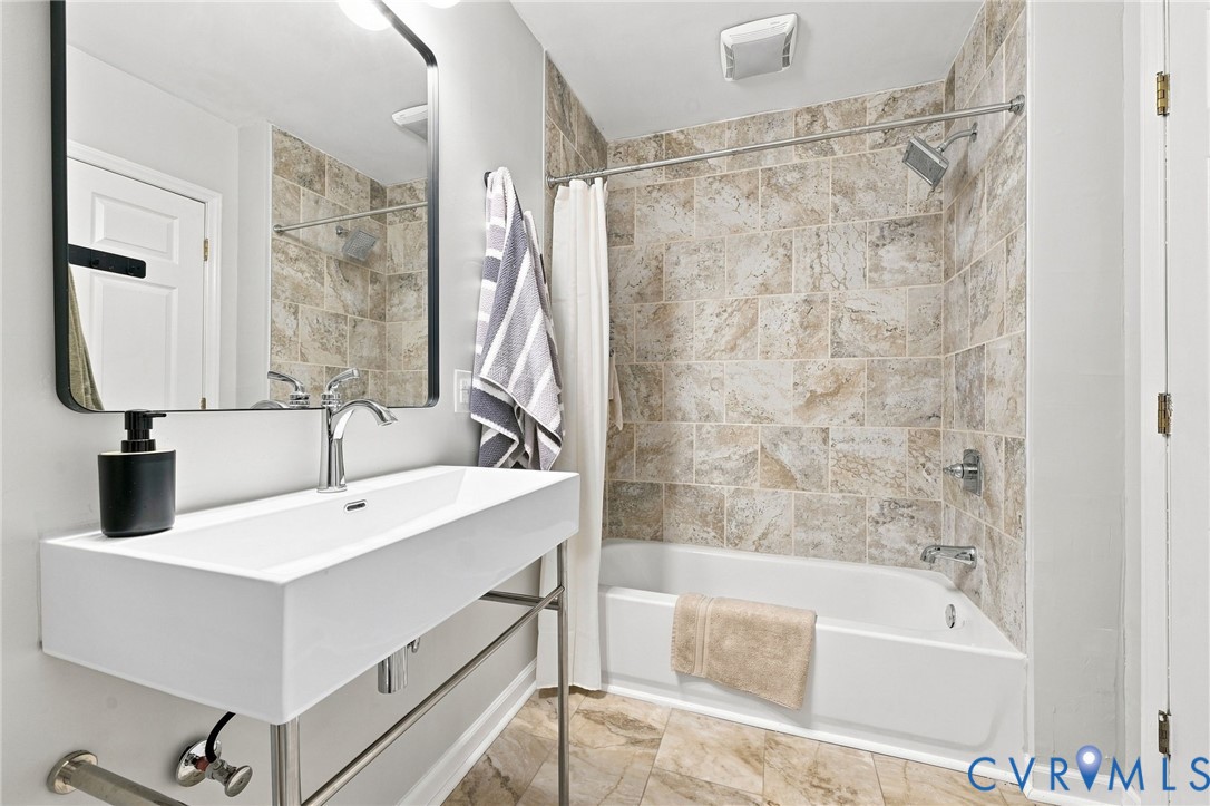 Bathroom with a floating sink and mirror beside a tub with beige tiled shower walls.