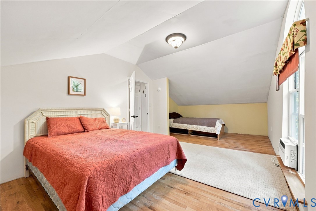 Attic bedroom with a coral-quilted bed, a second bed beneath the sloped ceiling, and hardwood floors.
