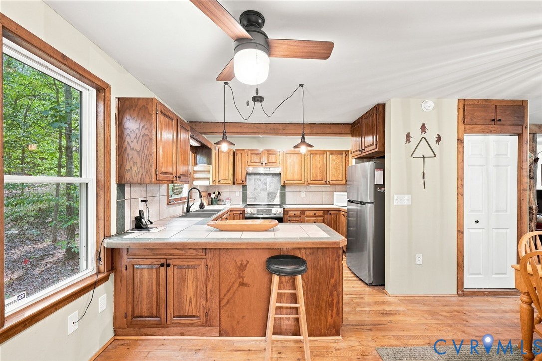 Kitchen with warm wood cabinets, tiled island, stainless steel appliances, and a large window overlooking trees.
