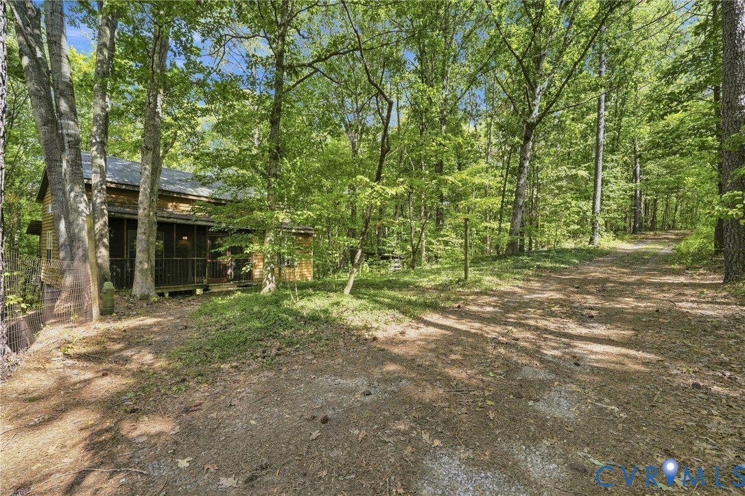 Wood-sided home with a covered porch tucked among trees beside a gravel driveway.