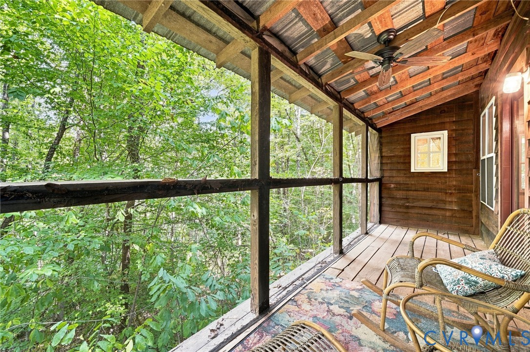 Screened wooden porch with wicker chairs, exposed beams, and a leafy woodland view.