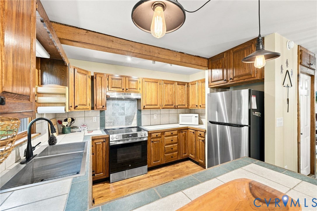 Kitchen with wooden cabinets, stainless steel appliances, tiled counters, and a deep sink.